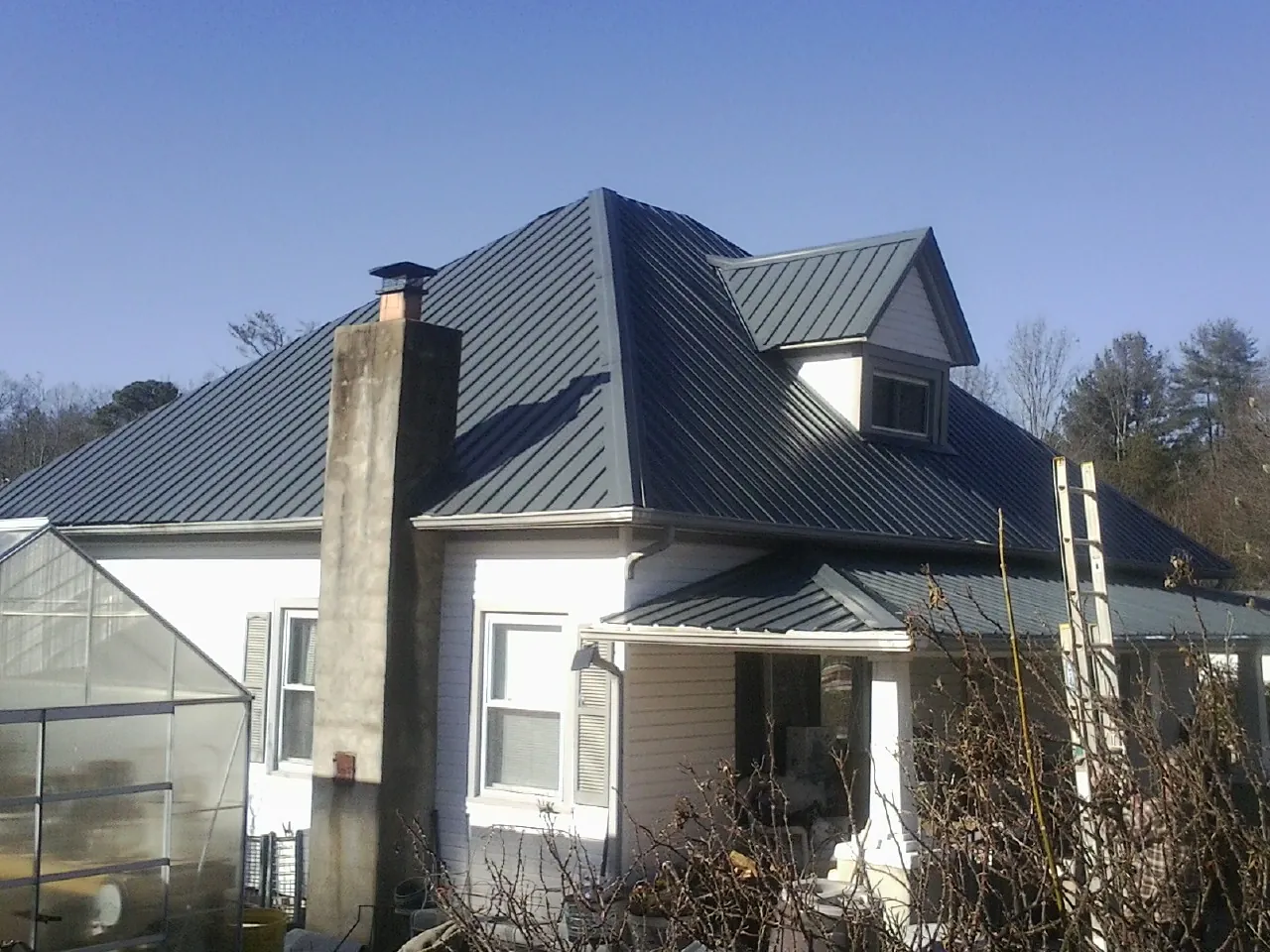 Dark blue standing seam metal roof on a white farmhouse with dormer — Slate & Tile Roof Repair by Roofing Brothers in Loma