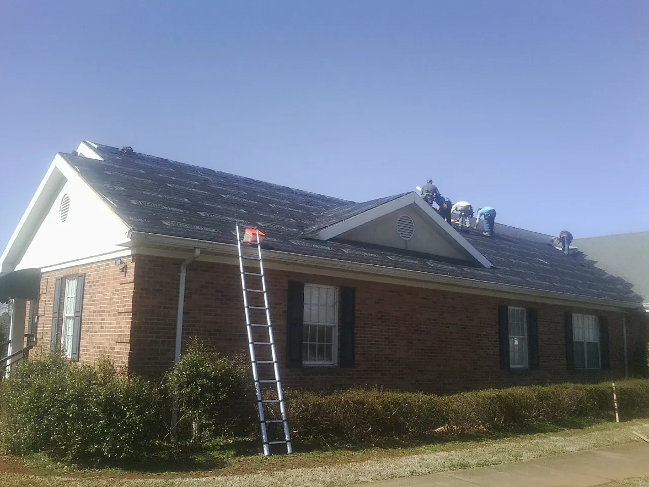 Crew tearing shingles off a brick ranch roof with a ladder set — Emergency Roof Repair work by our crew in Loma