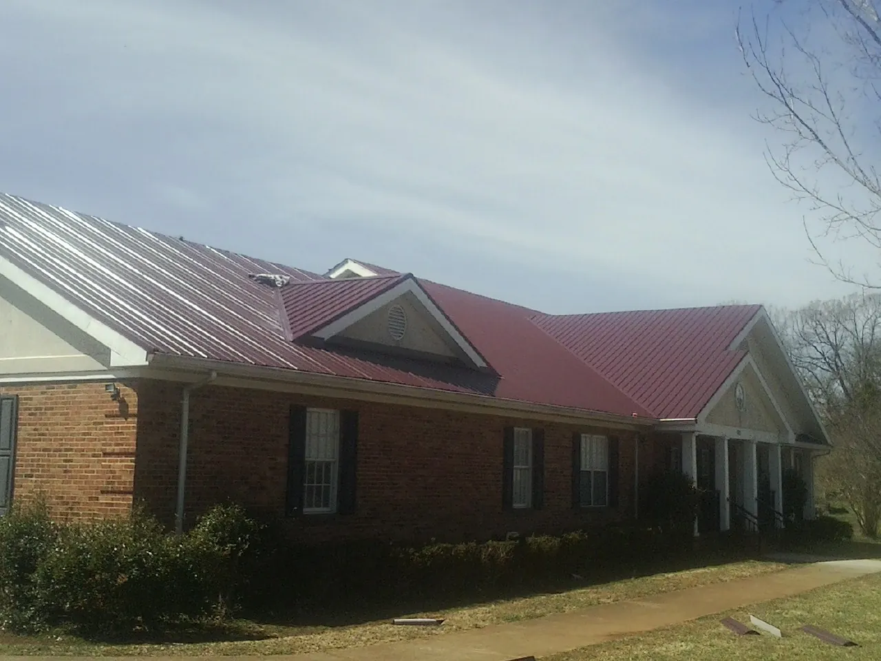Red metal roof with gabled entries on a long brick building, from a Hail Damage Roof Repair job in Loma