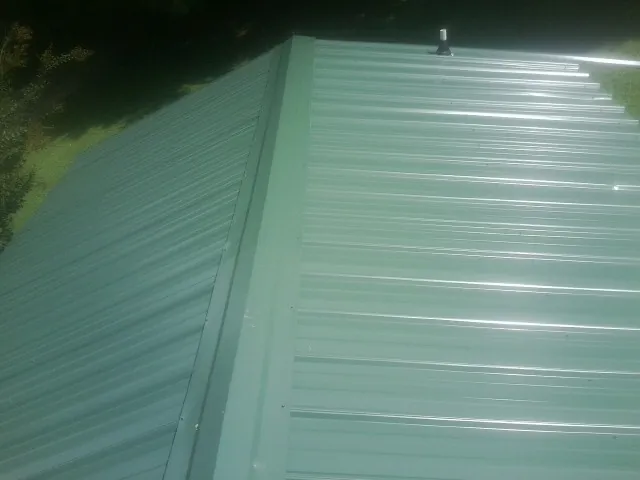 New green metal panels meeting at the ridge of a roof — Flat Roof Repair work by our crew in Loma
