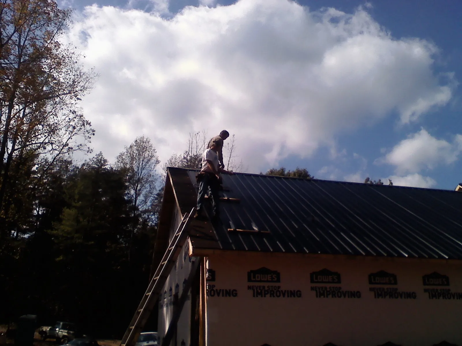 Roofer fastening dark metal panels high against a cloudy sky, from a Roof Inspection job in Loma