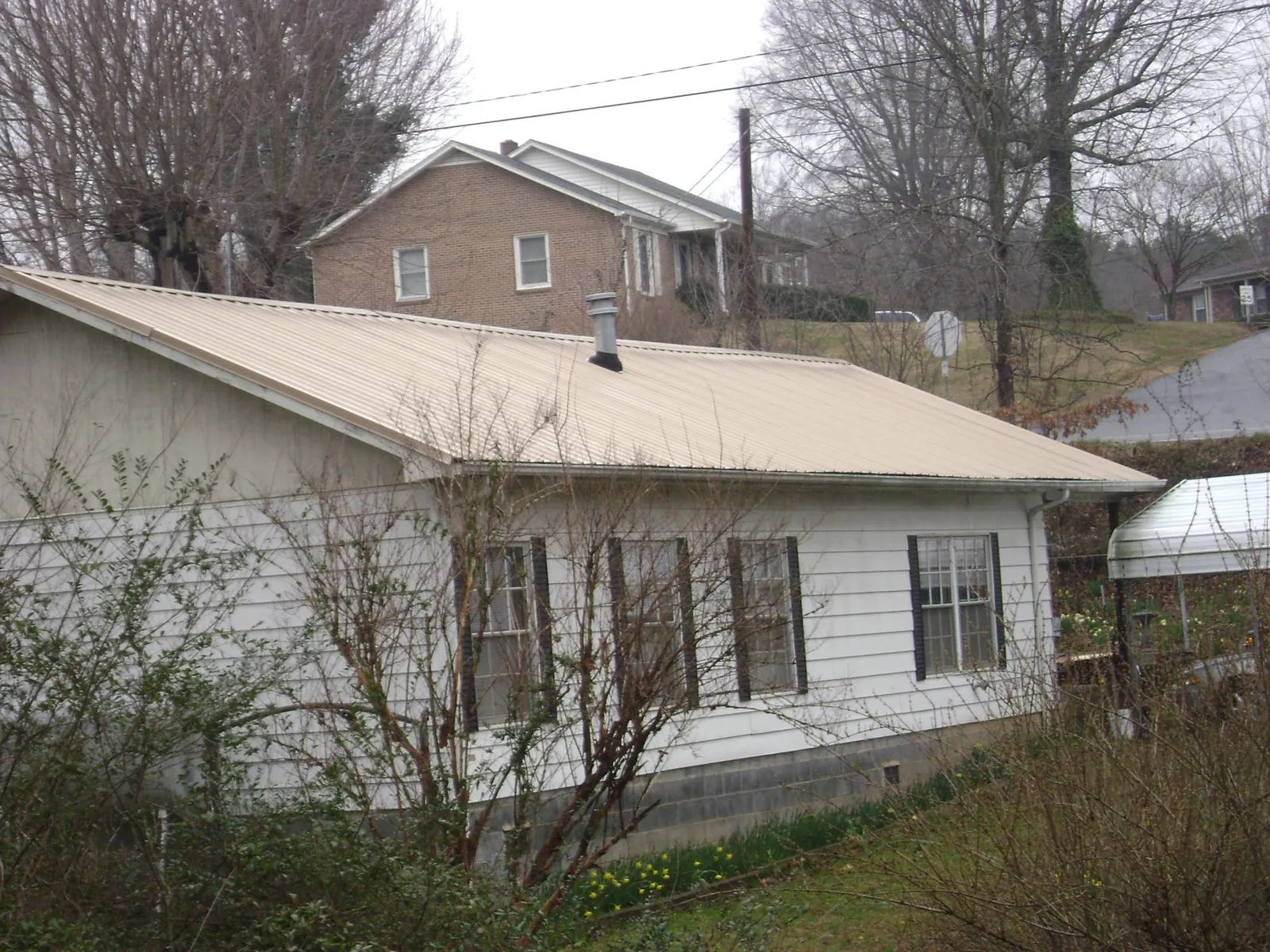 Tan metal roof on a white sided house set into a hillside — Commercial Roofing by Roofing Brothers in Loma