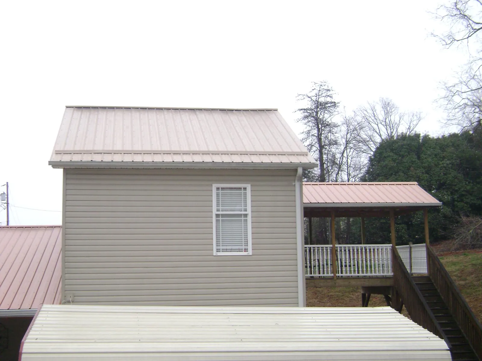 Tan metal roofs on a two story addition and attached porch, from a Roof Replacement job in Loma